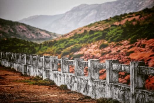Picturesque view of weathered symmetrical fence between bright dry sandy terrain and rough mounts with green grass in daylight