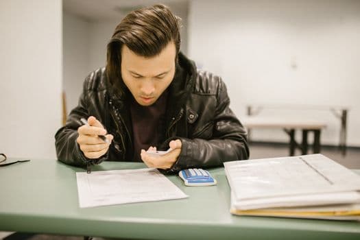 A male student in a classroom studying for an exam with a focus on his notes.