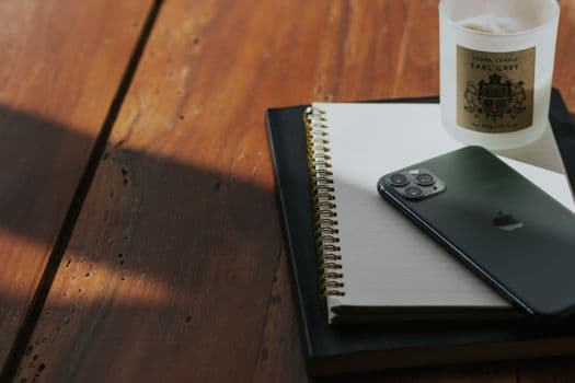 Modern workspace setup with a smartphone, notebook, and candle on a wooden desk.