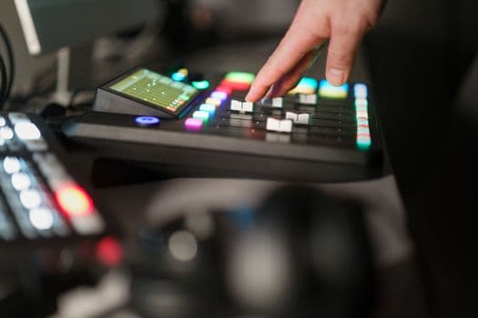 A hand adjusts controls on an illuminated sound mixer console in a recording studio setting.