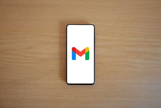 A smartphone displaying the Gmail app logo on a wooden surface, viewed from above.
