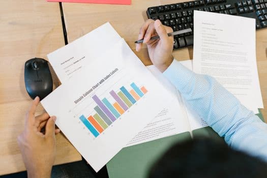 A business analyst reviews a colorful bar chart and documents at a desk, indicating data analysis.