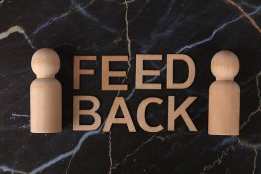 Wooden letters spelling 'Feedback' with peg-like figures on marble background.