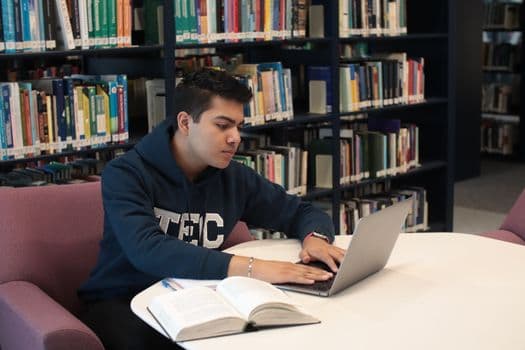 Student in library using laptop and textbooks for study and research.
