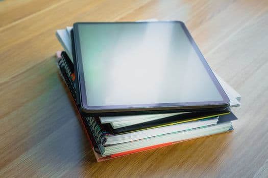 Digital tablet resting on top of a stack of books, depicting modern education and technology.
