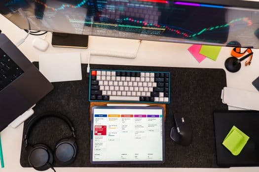 Top view of a tech workspace featuring a digital tablet, keyboard, monitor, and headphones for project management.