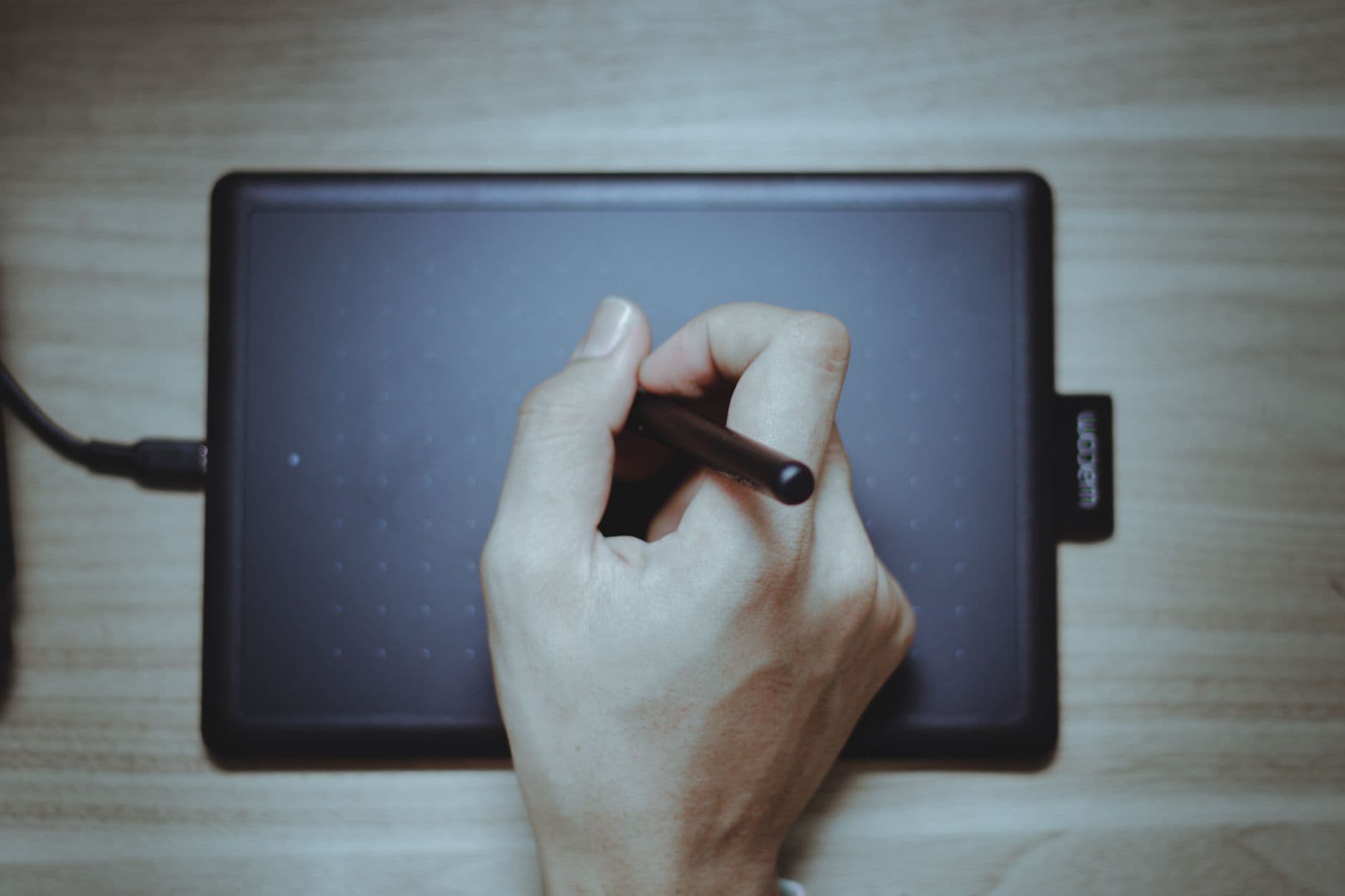 Hand using a stylus on a digital drawing tablet, top view.