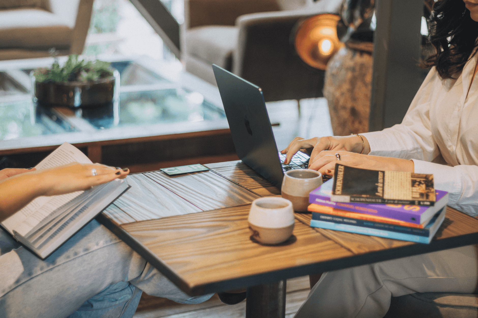 Two people working in a cozy setting with laptops and books, fostering collaboration.