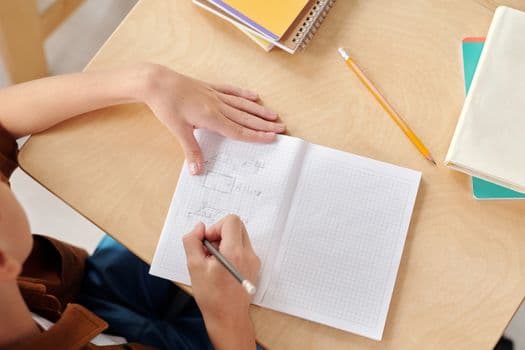 Young student writing math equations in a notebook at school desk.