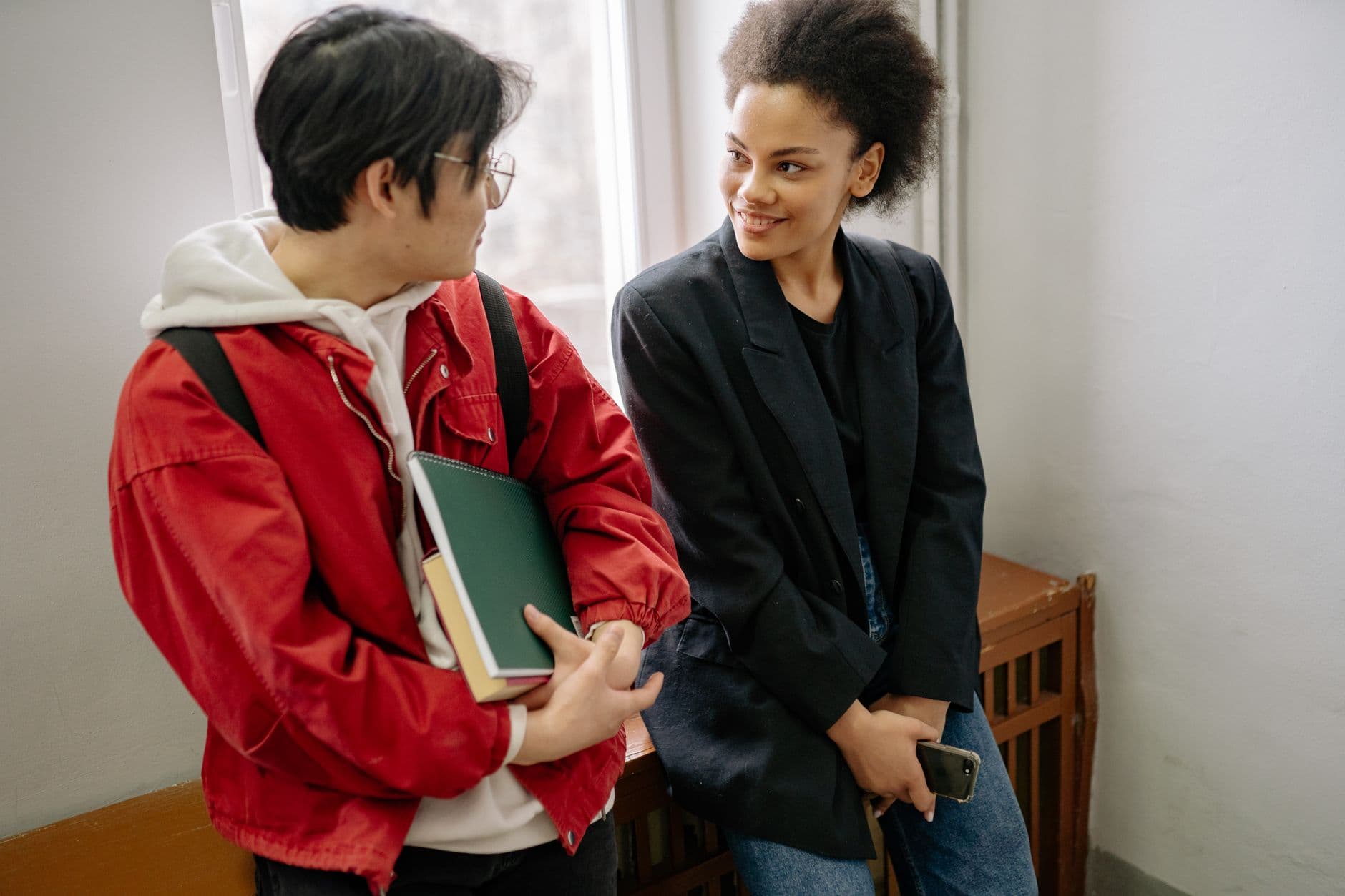 Two teenagers smiling and talking in a bright school corridor.