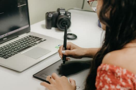 A woman using a digital tablet and stylus next to a laptop, showcasing modern design technology.