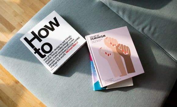 A collection of books on feminism and design resting on a stylish sofa.