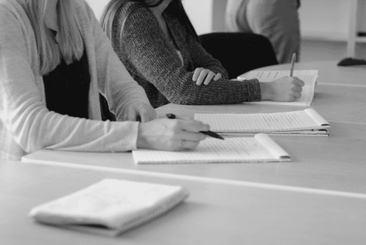 Black and white image of students writing notes during a meeting.