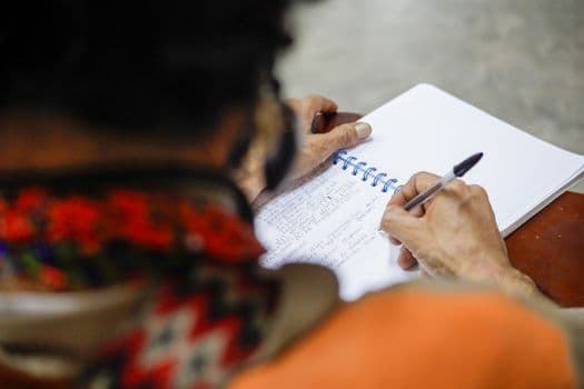 Close-up of a person writing in a spiral notebook with a ballpoint pen.