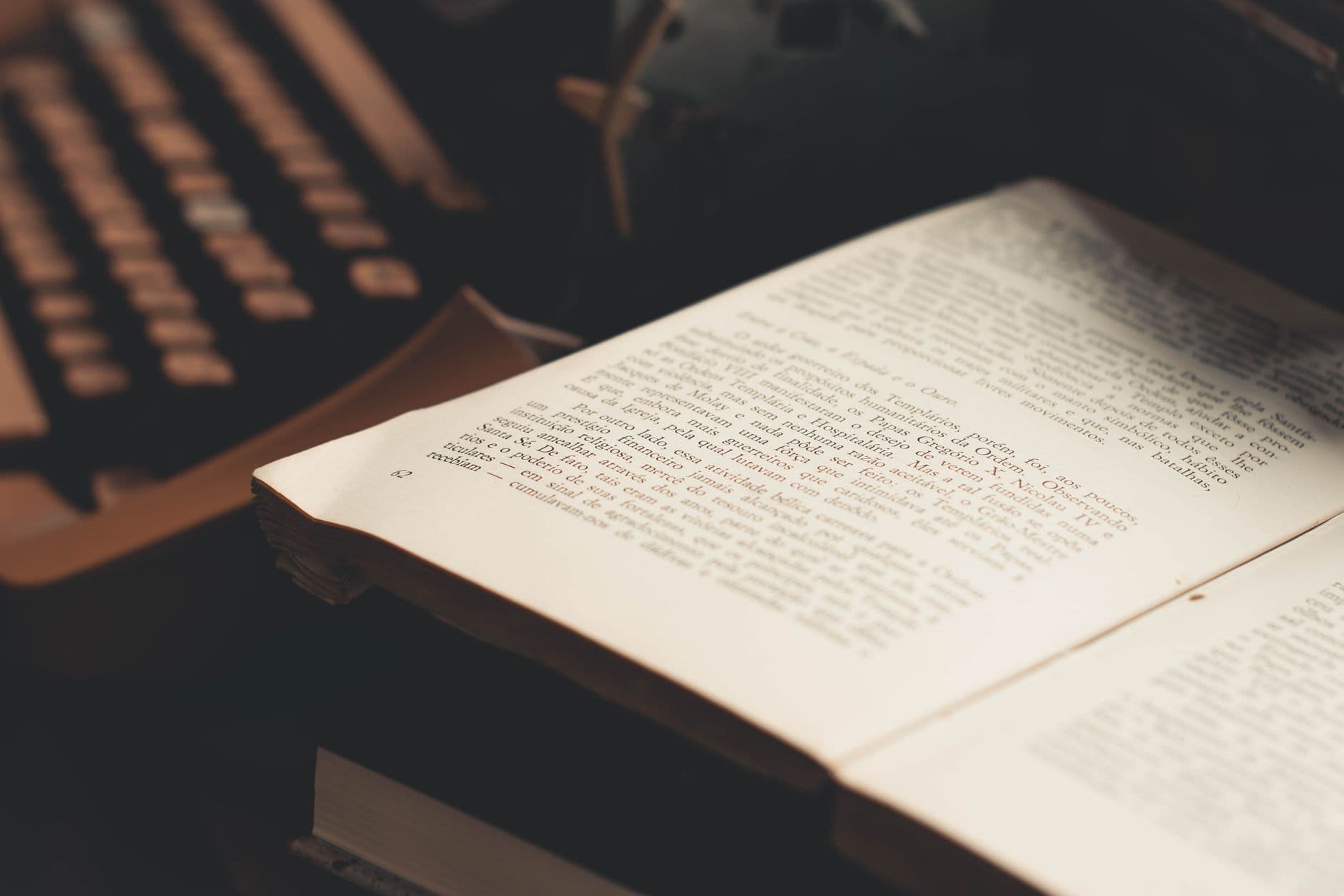 An open book with visible text in front of an antique typewriter, evoking a vintage literary theme.