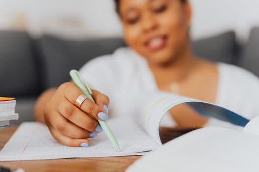 A close-up of a focused woman writing notes while studying indoors, emphasizing learning.