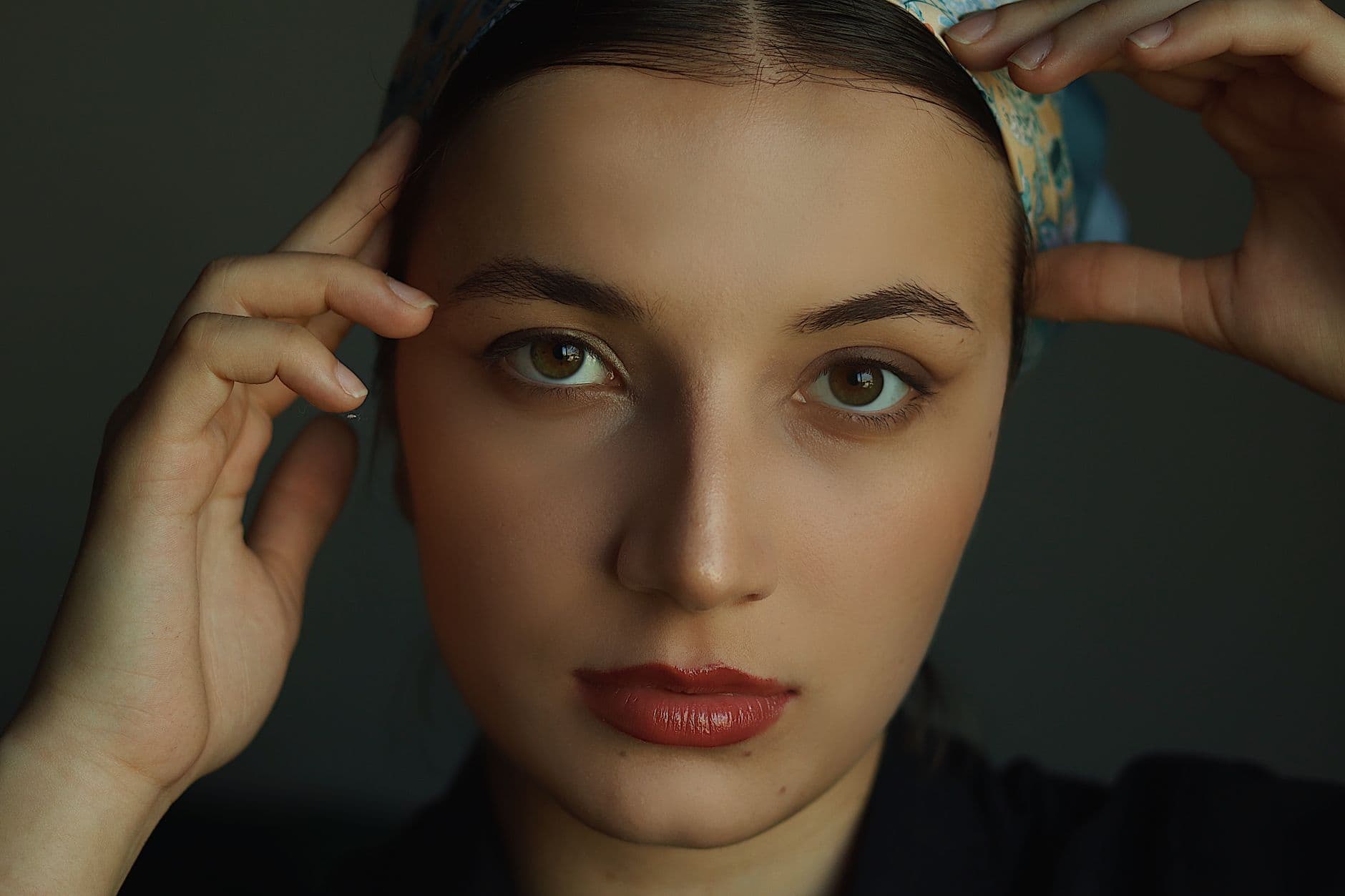 A captivating close-up portrait of a woman with a serious expression and hands on head.